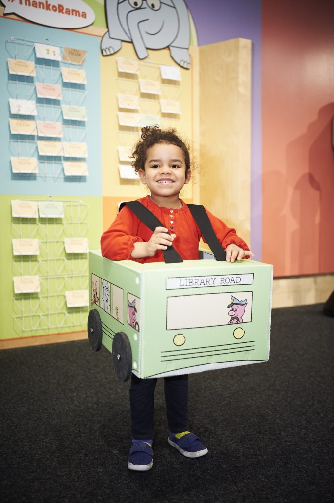 Photo of a child inside the pigeon exhibit wearing a cardboard bus costume