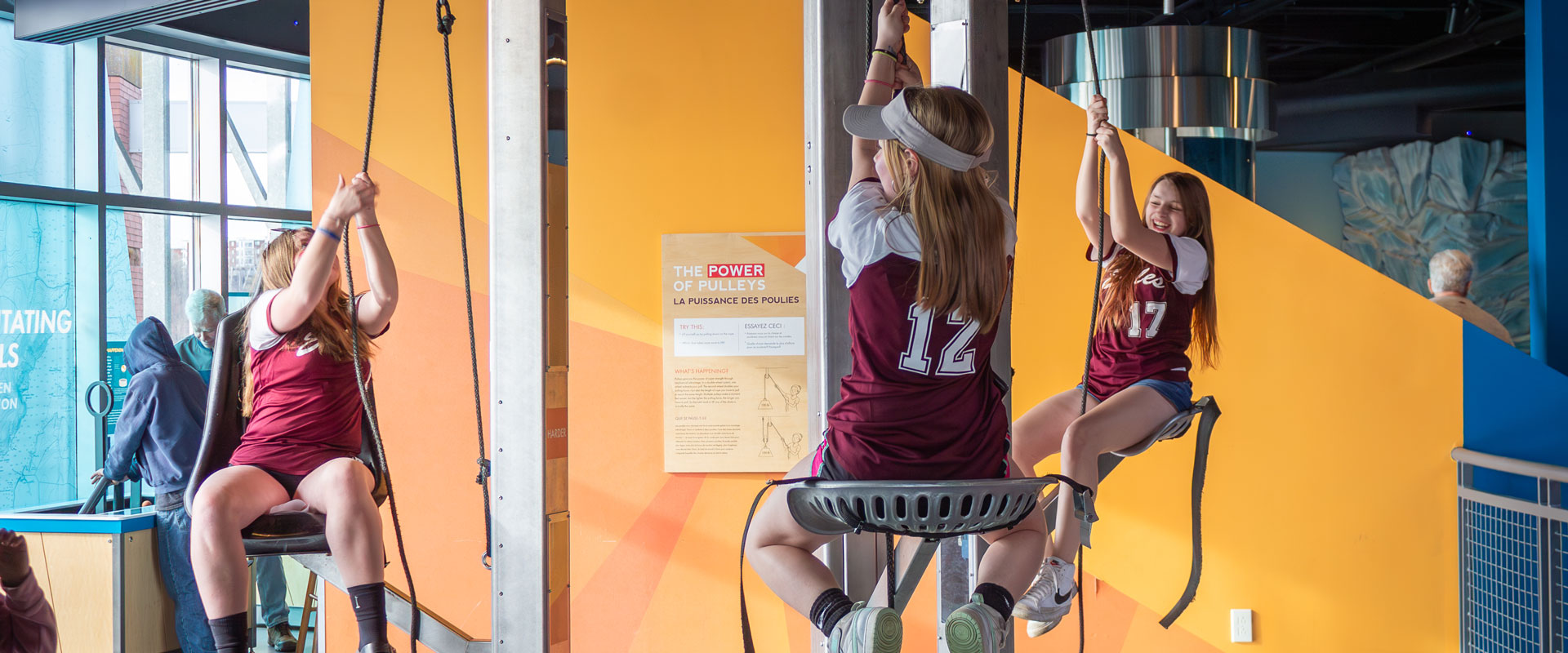 Three students in sports uniforms pulling themselves up on ECHO's pulley chairs