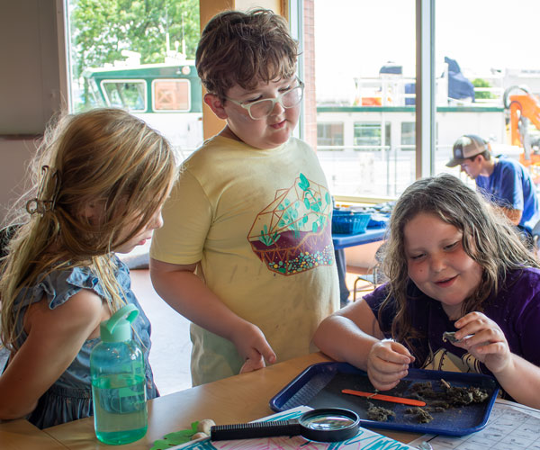 Three campers gather around to inspect the contents of an owl pellet