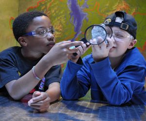 Two campers use a magnifying glass to inspect a rock