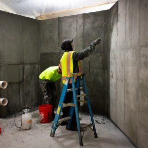 Two contractors spray waterproofing solution inside ECHO's new Lake Tank