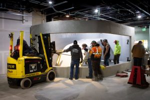 Several workers gather around the concrete shell of ECHO's new 15,000-gallon Lake Tank. Inside the tank, a giant piece of acrylic wrapped in protective plastic is waiting to be lifted into place in the tank's viewing window.