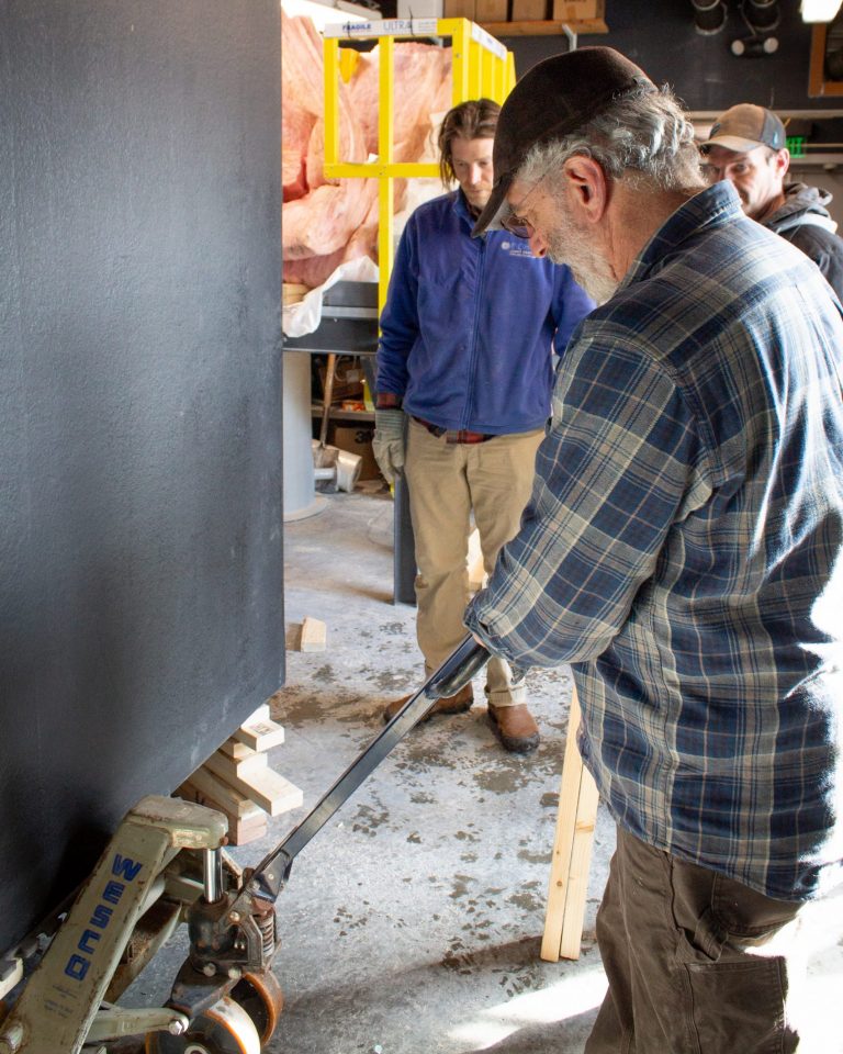 ECHO Facilities and Animal Care Director Steve uses a pallet jack to lift a large black tank into position while two employees watch.